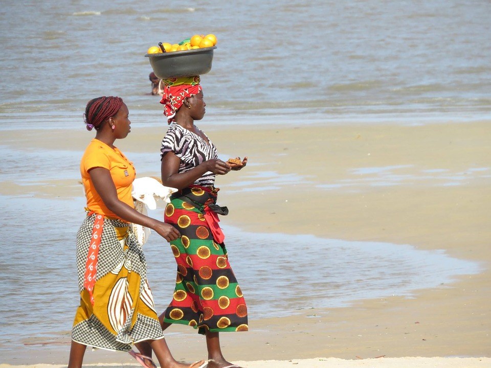 Mozambican women walking on beach carrying fruit 